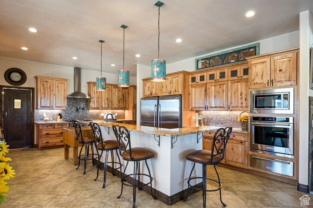 Kitchen featuring stainless steel appliances, wall chimney exhaust hood, a warming drawer, backsplash, and recessed lighting