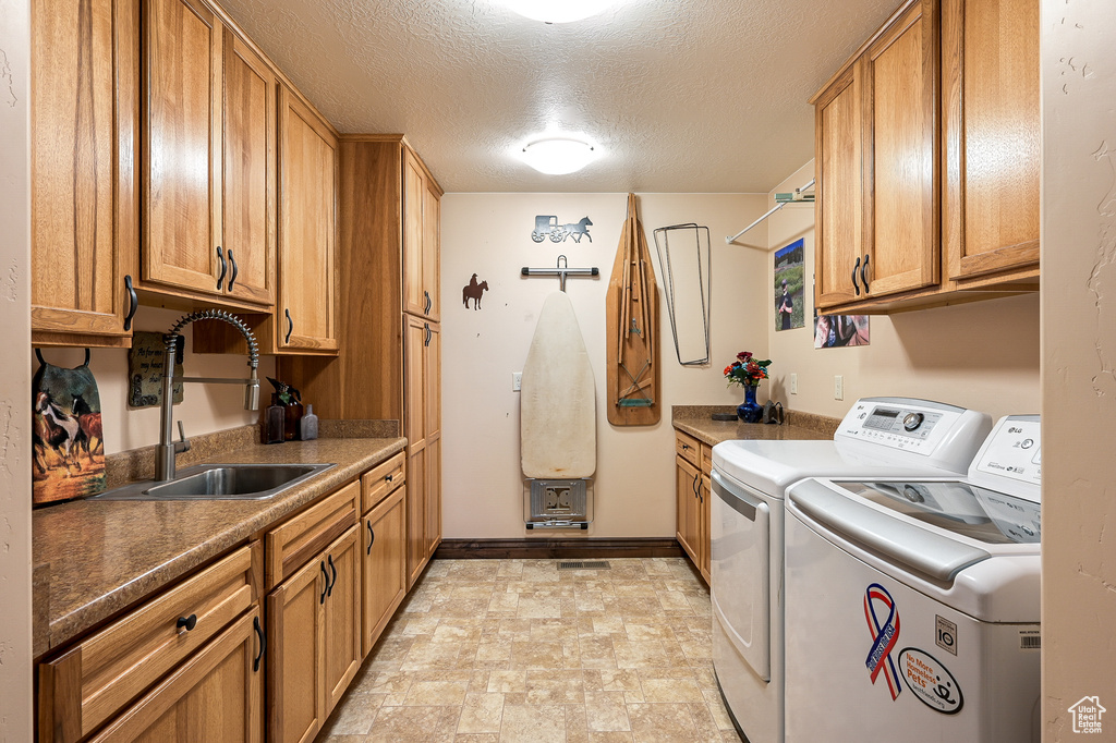 Laundry area featuring washer and dryer, cabinet space, a textured ceiling, stone finish floors, and baseboards