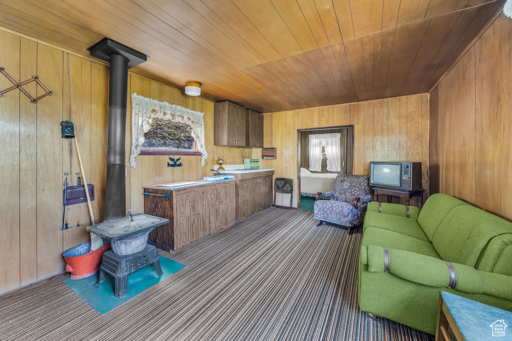 Living room with a wood stove, wooden ceiling, wooden walls, and carpet floors