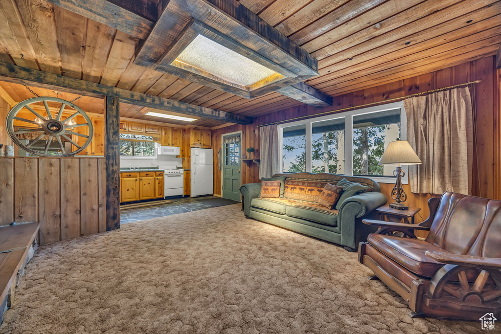 Living area featuring wood ceiling, wood walls, beamed ceiling, dark carpet, and a skylight