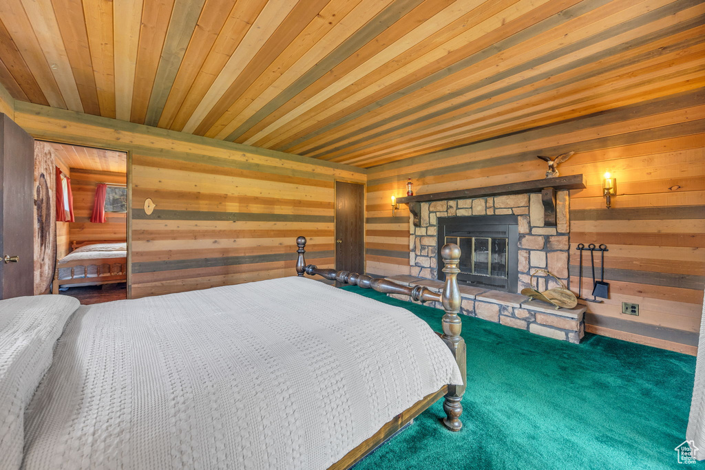 Carpeted bedroom featuring wooden walls, wood ceiling, and a fireplace