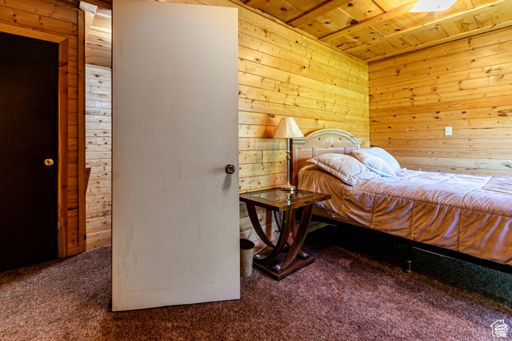 Bedroom with wooden ceiling, wooden walls, and carpet