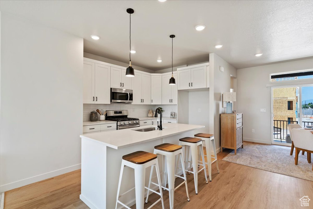 Kitchen featuring stainless steel appliances, light wood-type flooring, tasteful backsplash, light countertops, and a kitchen bar