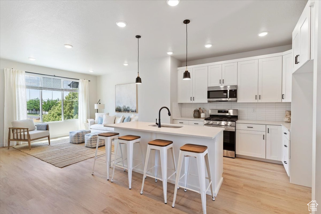 Kitchen with appliances with stainless steel finishes, open floor plan, light wood finished floors, backsplash, and a kitchen breakfast bar