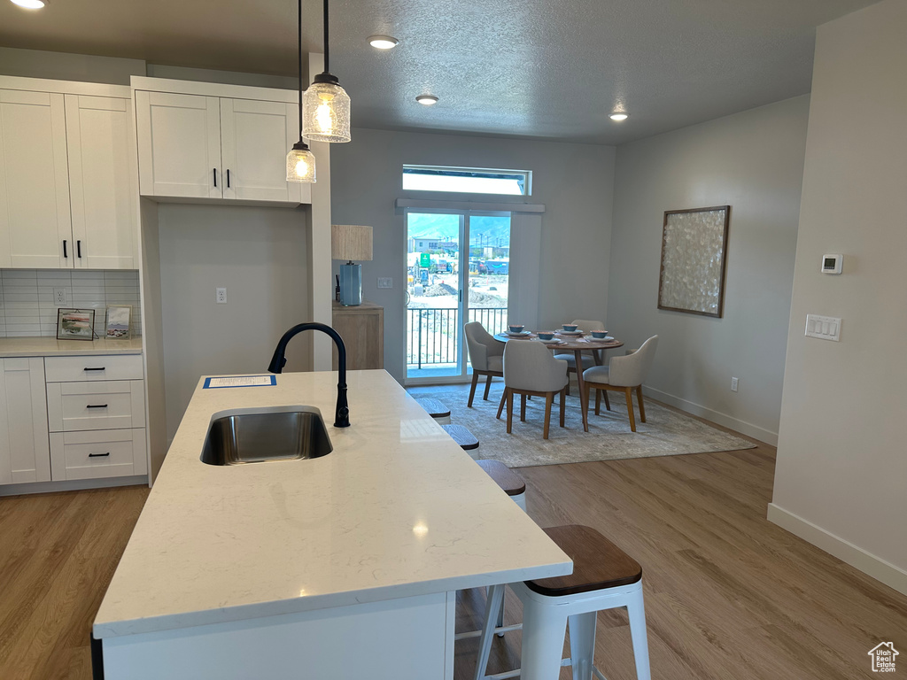 Kitchen featuring a sink, white cabinets, baseboards, a kitchen island with sink, and light wood-style flooring