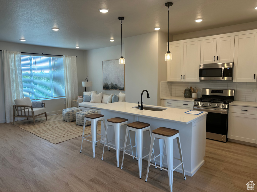 Kitchen with appliances with stainless steel finishes, a sink, light wood-type flooring, a breakfast bar area, and decorative backsplash