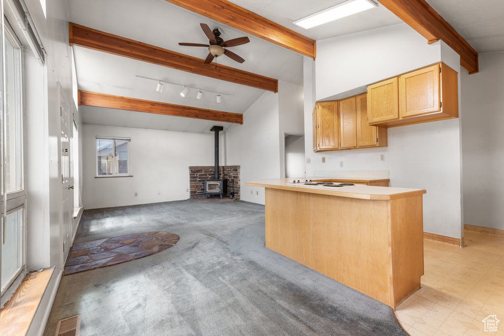 Kitchen featuring a wood stove, beam ceiling, a ceiling fan, white stovetop, and open floor plan