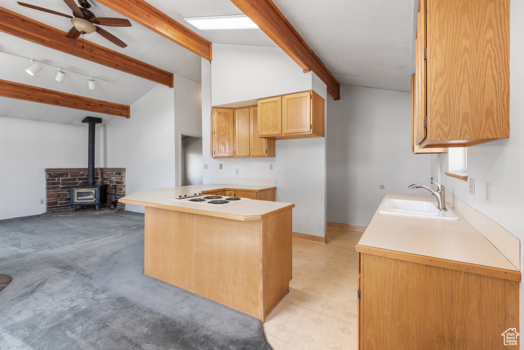 Kitchen featuring a sink, white electric stovetop, a ceiling fan, a wood stove, and light countertops