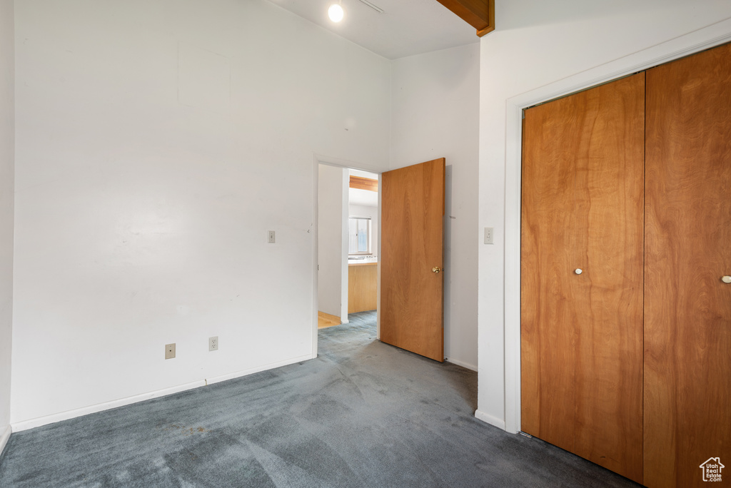 Unfurnished bedroom featuring carpet floors, baseboards, a closet, and a towering ceiling