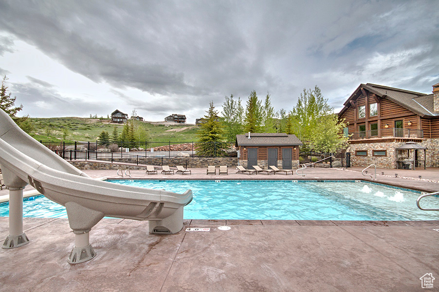 Community pool featuring fence, a water slide, and a patio