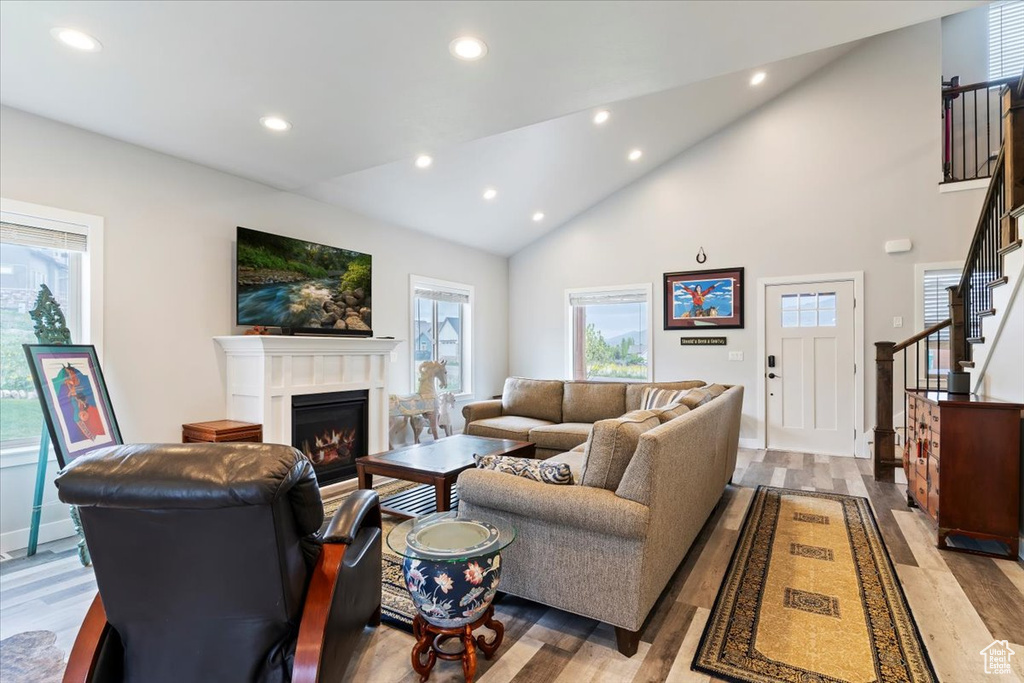 Living area featuring recessed lighting, a glass covered fireplace, light wood-style flooring, stairs, and high vaulted ceiling