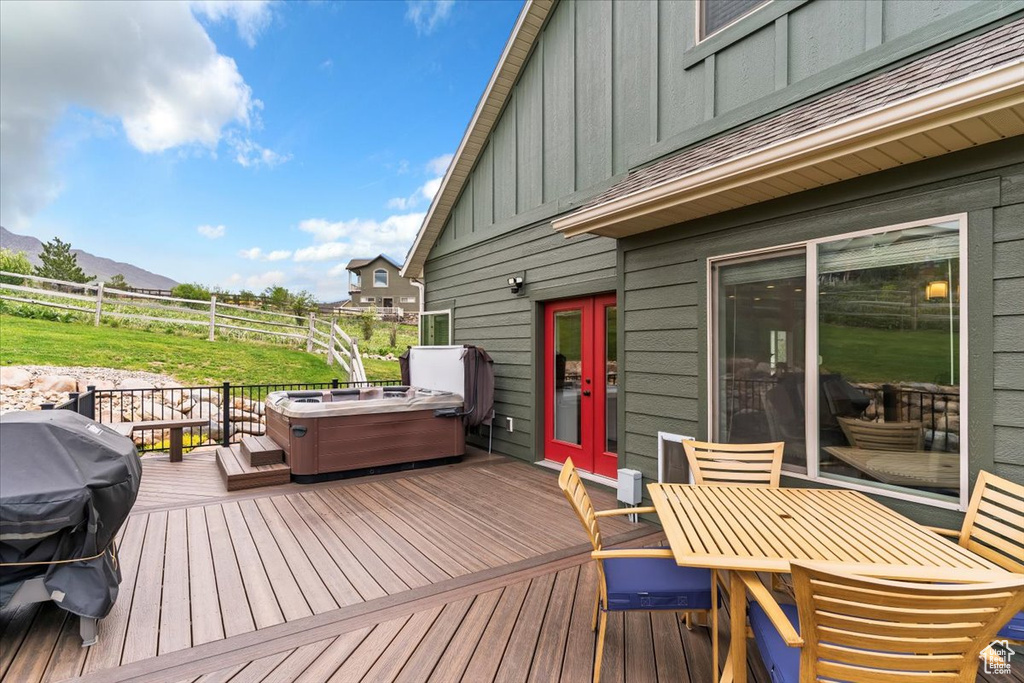 Wooden terrace featuring a hot tub, outdoor dining space, a mountain view, grilling area, and fence