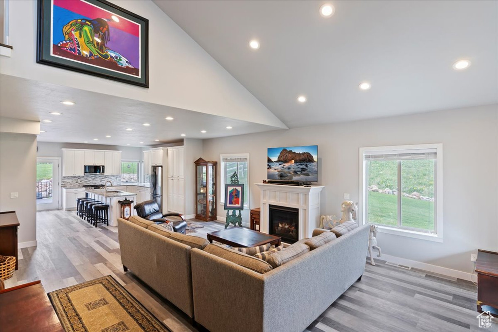 Living room with a lit fireplace, recessed lighting, light wood-type flooring, baseboards, and high vaulted ceiling