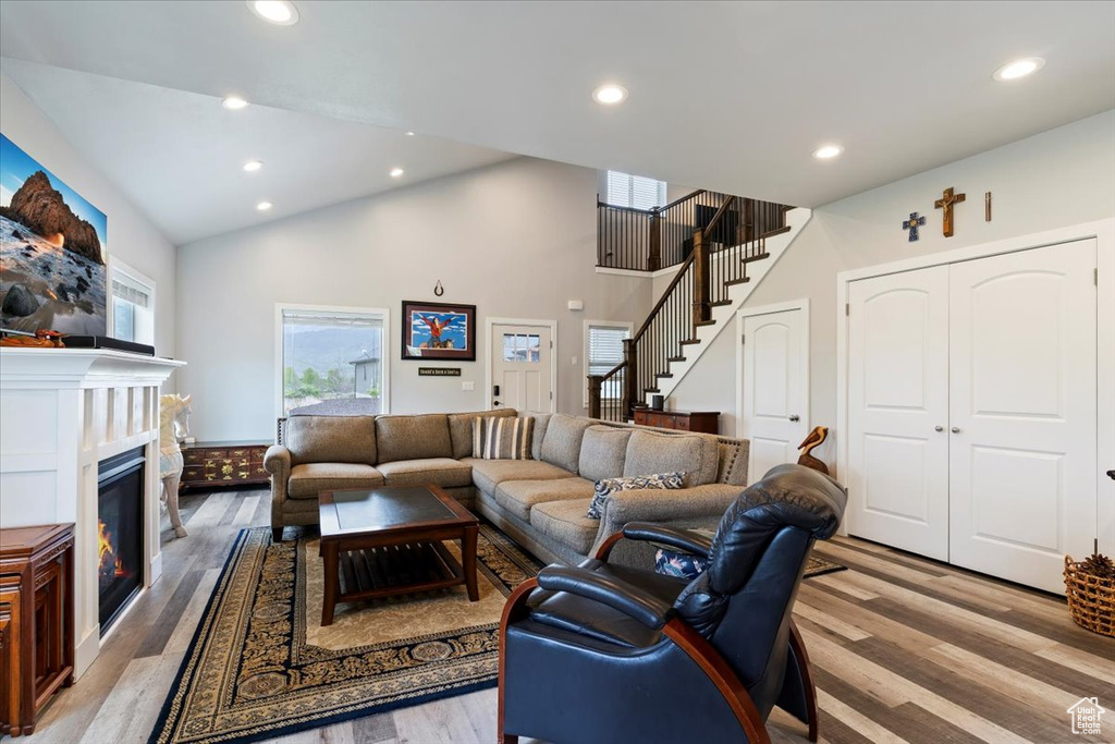 Living room with wood finished floors, stairway, recessed lighting, high vaulted ceiling, and a glass covered fireplace