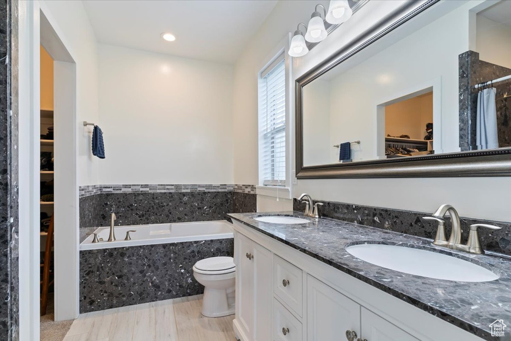 Bathroom featuring a walk in closet, a garden tub, double vanity, recessed lighting, and toilet