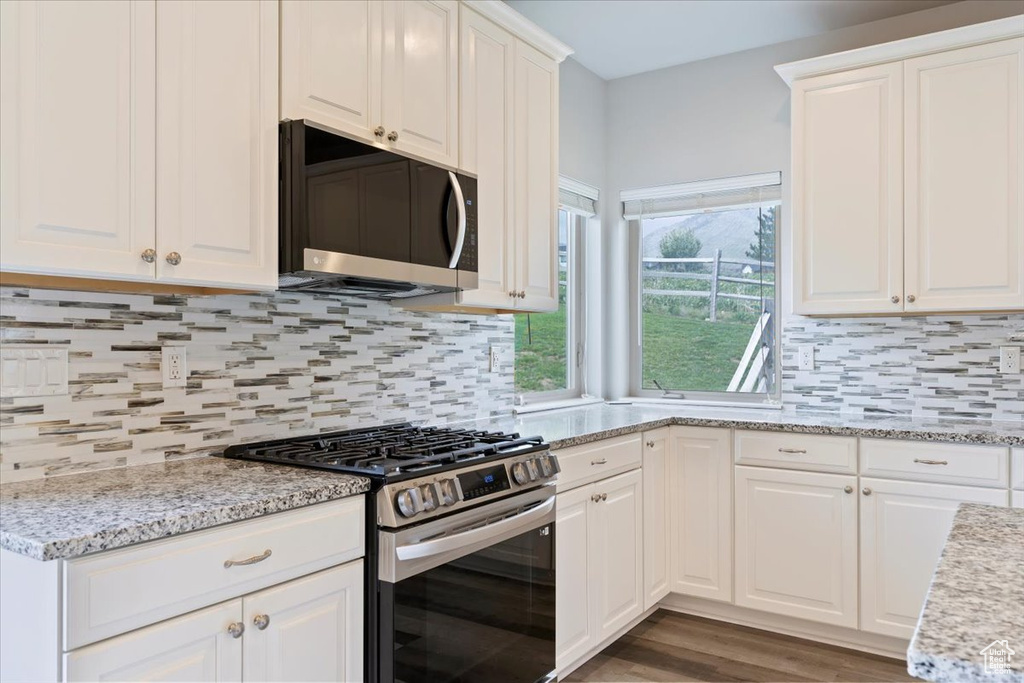 Kitchen featuring stainless steel appliances, white cabinets, backsplash, light stone countertops, and wood finished floors