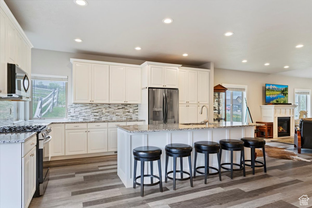 Kitchen with appliances with stainless steel finishes, a sink, backsplash, light wood-style floors, and white cabinetry