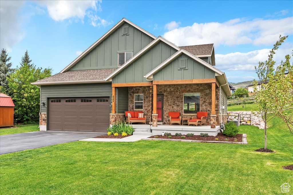 Craftsman house featuring a porch, board and batten siding, asphalt driveway, an attached garage, and a front yard