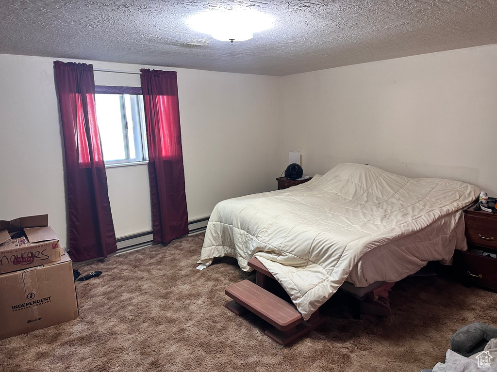 Bedroom with carpet, baseboard heating, and a textured ceiling