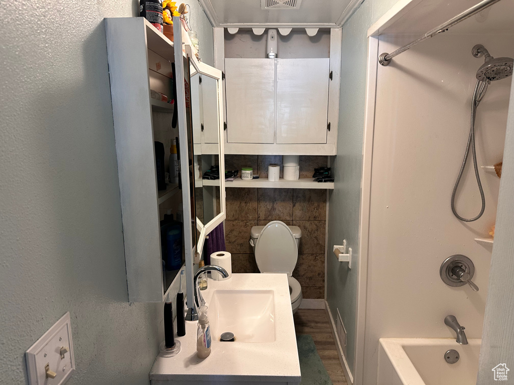 Full bath with a sink, toilet,  shower combination, and wood finished floors