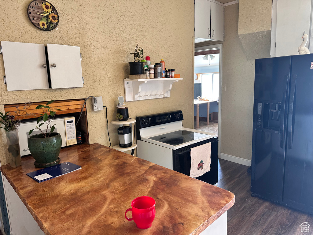 Kitchen with black fridge with ice dispenser, range with electric stovetop, dark wood-style flooring, white cabinetry, and baseboards