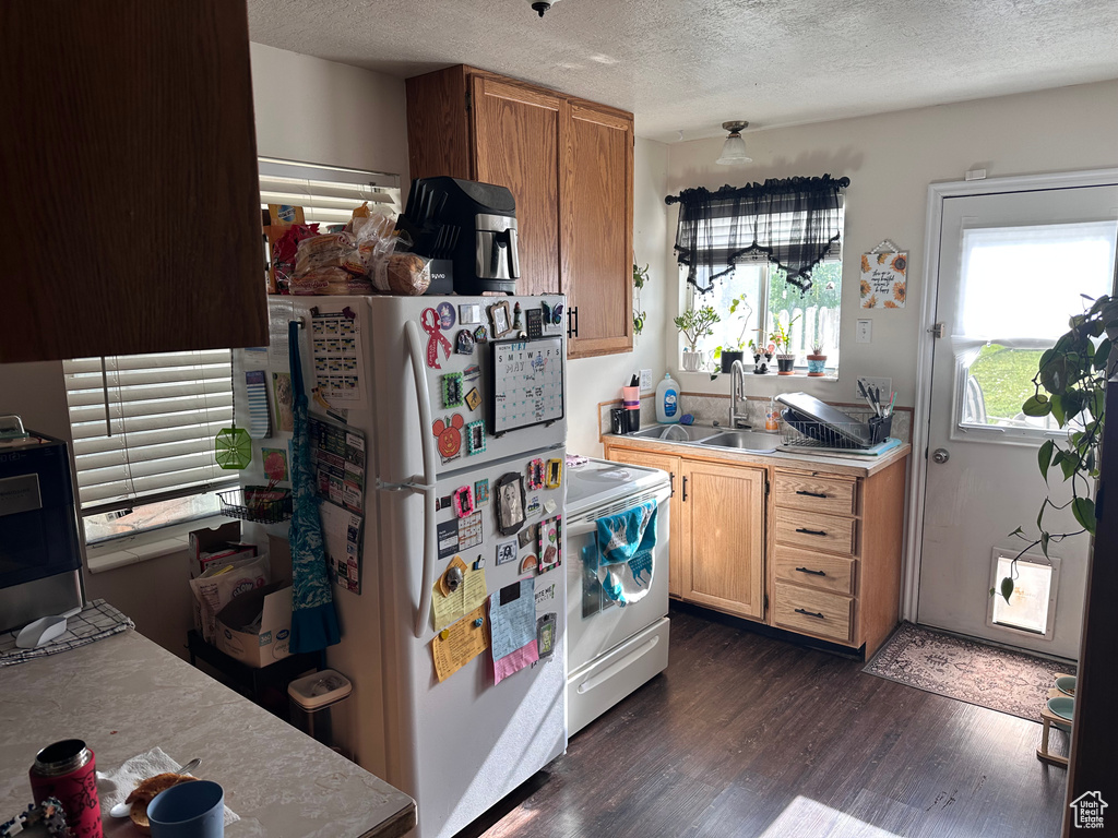 Kitchen with white appliances, a sink, dark wood-style flooring, a textured ceiling, and light countertops