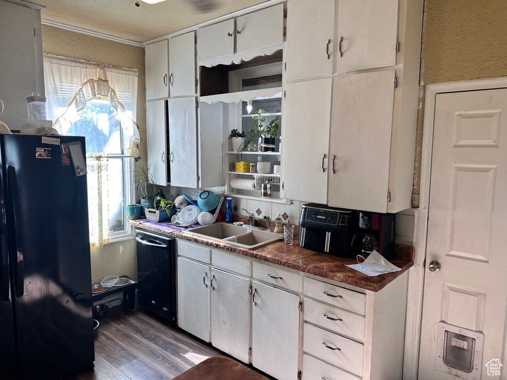 Kitchen with black appliances, a sink, dark wood-style flooring, a textured wall, and dark countertops