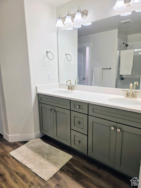 Bathroom with wood finished floors, double vanity, a shower, and baseboards
