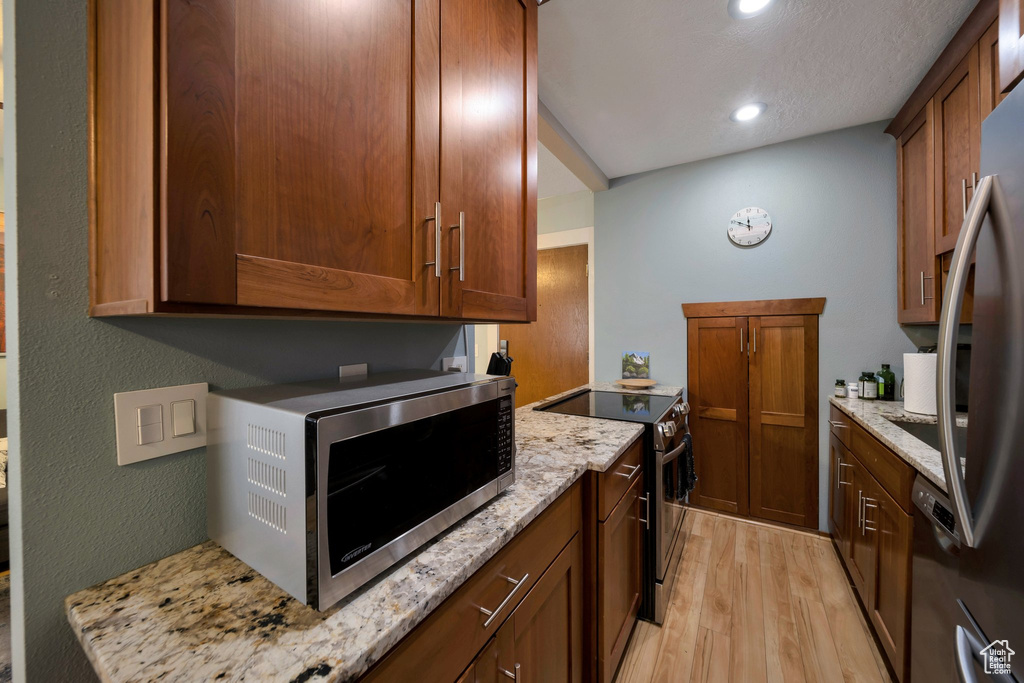 Kitchen featuring appliances with stainless steel finishes, light wood-style flooring, light stone countertops, recessed lighting, and brown cabinetry