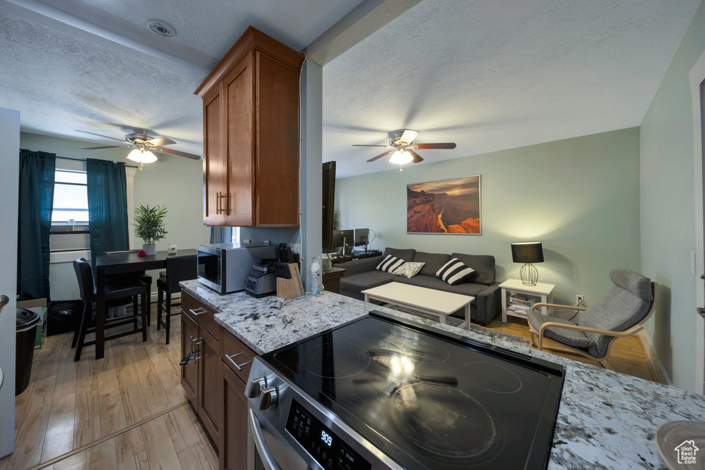 Kitchen featuring range with electric cooktop, a ceiling fan, stainless steel microwave, a textured ceiling, and light stone counters