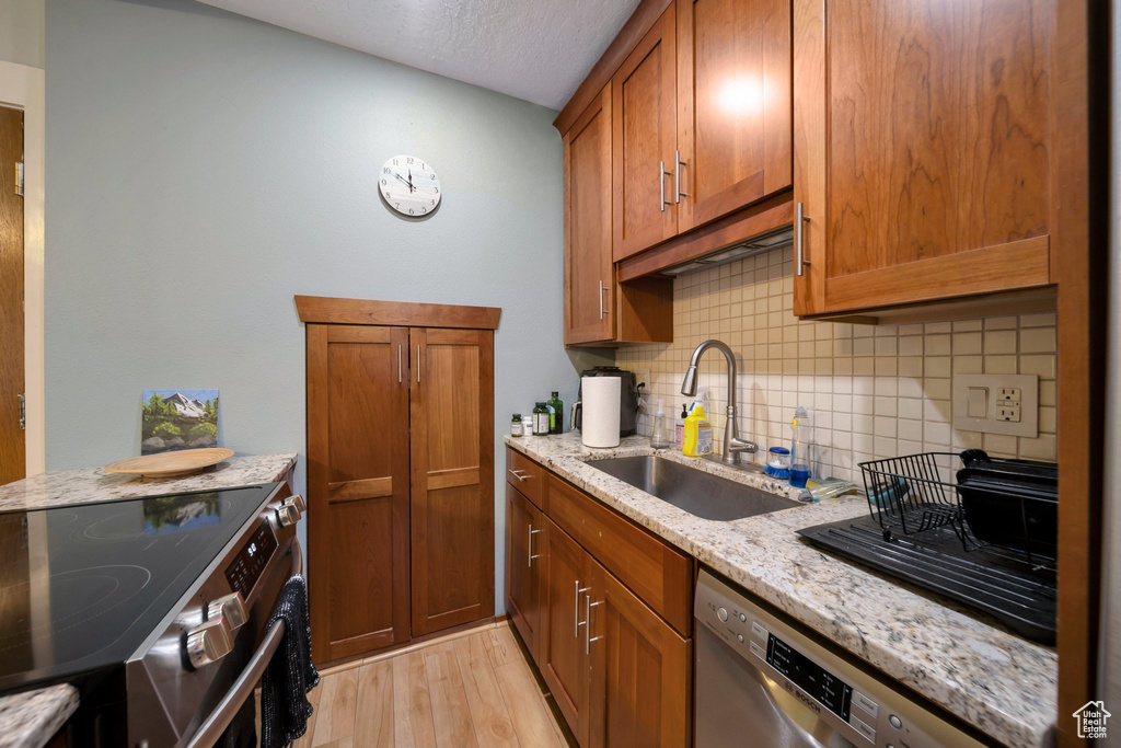 Kitchen with stainless steel appliances, a sink, decorative backsplash, brown cabinets, and light wood-type flooring