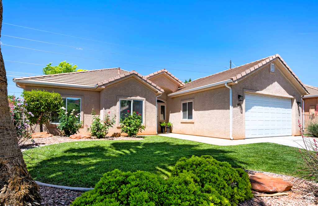 Ranch-style house featuring an attached garage, stucco siding, a front lawn, a tiled roof, and driveway