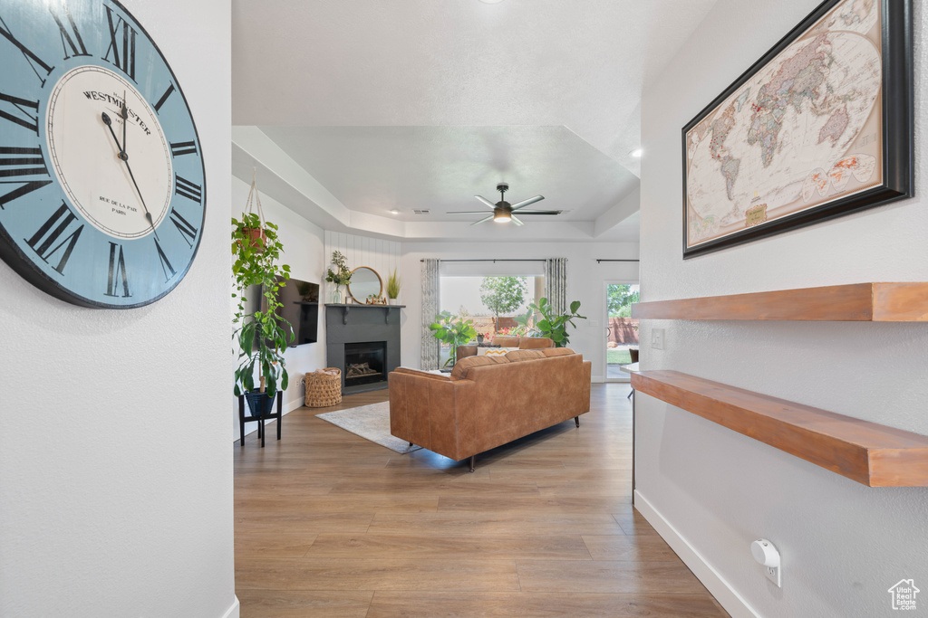Living area with a glass covered fireplace, a raised ceiling, wood finished floors, baseboards, and recessed lighting