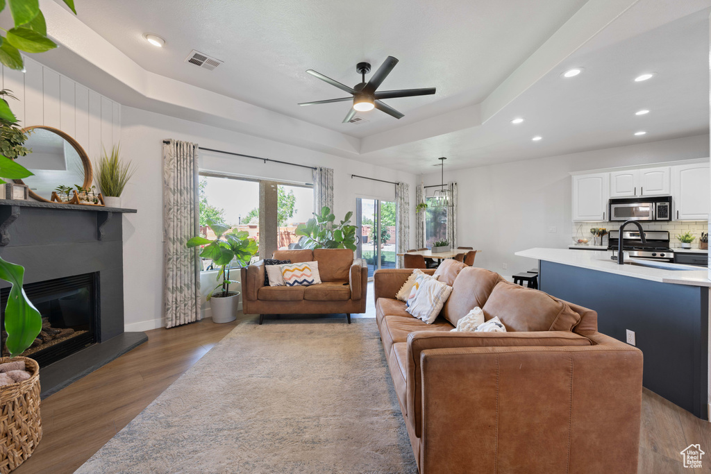 Living area featuring recessed lighting, wood finished floors, a ceiling fan, a raised ceiling, and a fireplace