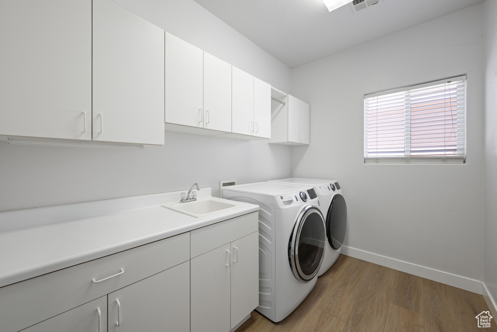 Laundry area with cabinet space, light wood finished floors, washer and dryer, and baseboards