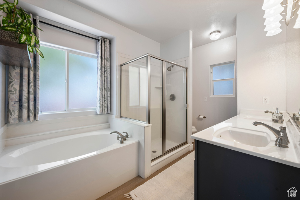 Full bath with a stall shower, a bath, wood finished floors, and double vanity