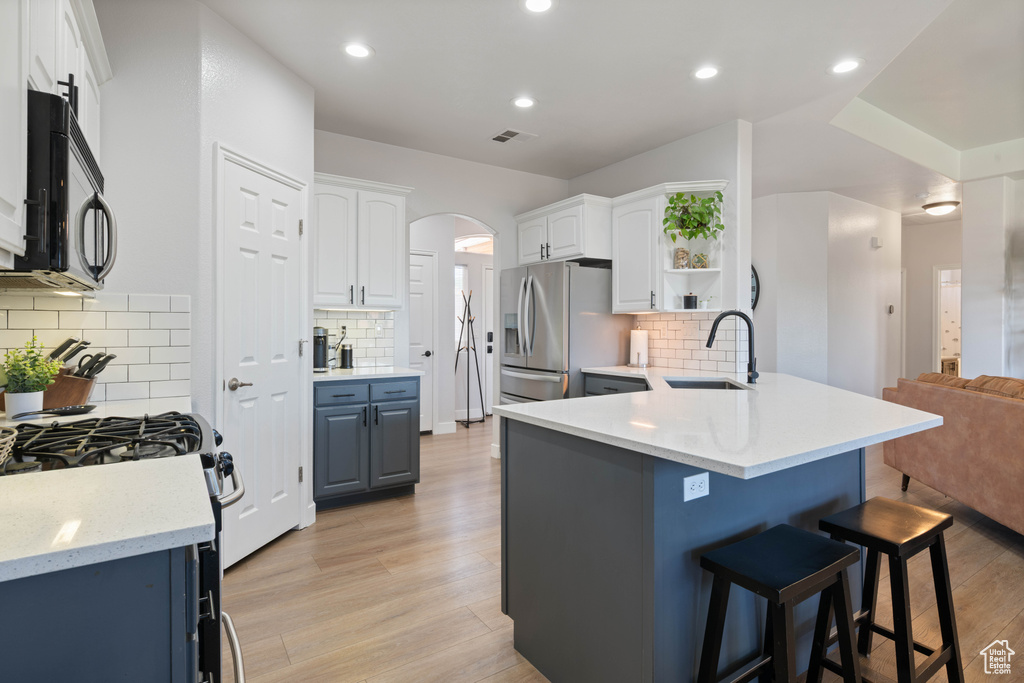 Kitchen featuring a sink, black microwave, stainless steel refrigerator with ice dispenser, a kitchen bar, and a peninsula