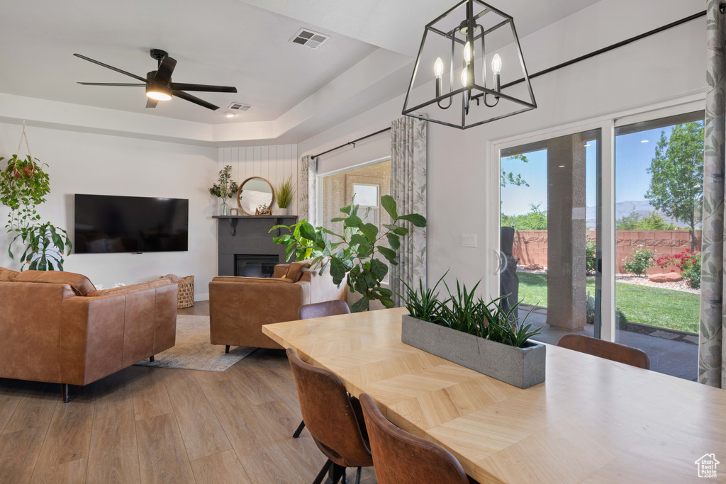 Dining space featuring wood finished floors, a ceiling fan, a chandelier, and a glass covered fireplace