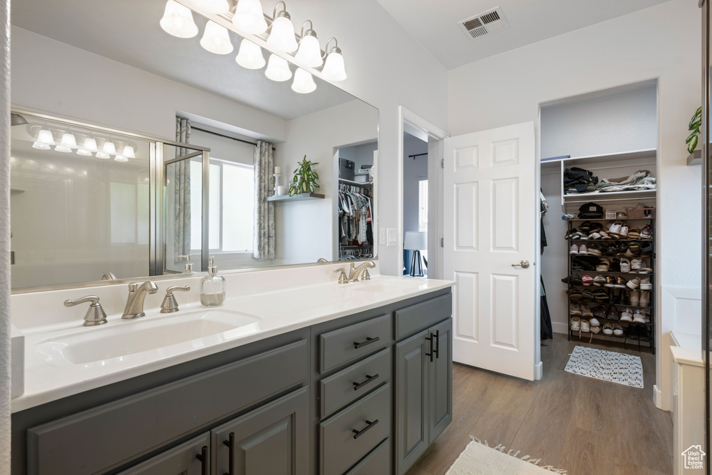 Bathroom featuring wood finished floors, double vanity, a walk in closet, and a shower with shower door