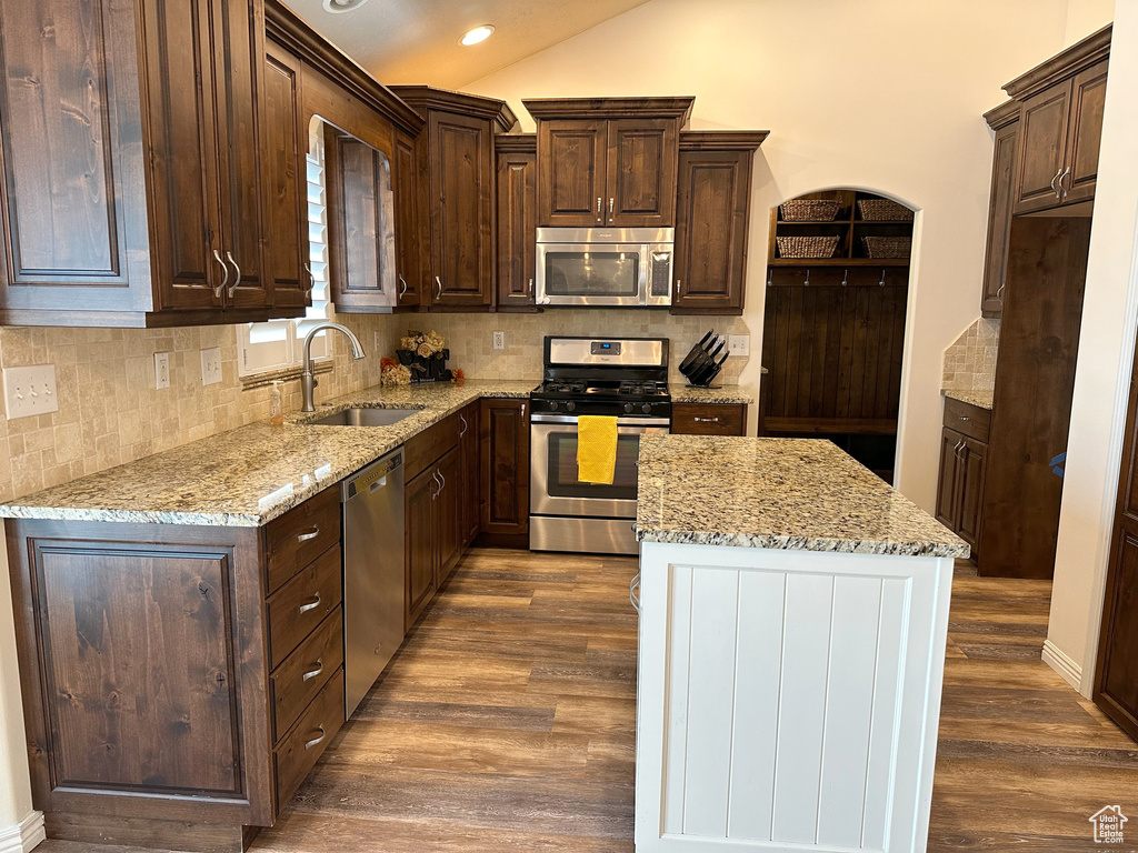 Kitchen with stainless steel appliances, a sink, dark brown cabinetry, dark wood-style flooring, and vaulted ceiling
