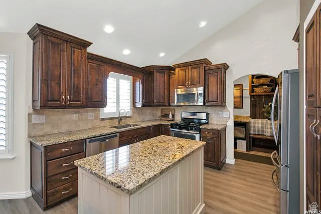 Kitchen with appliances with stainless steel finishes, a sink, tasteful backsplash, light wood finished floors, and lofted ceiling