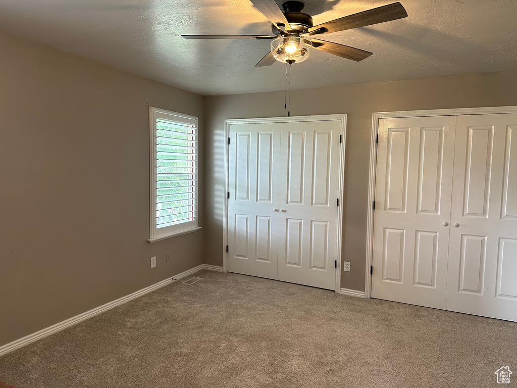 Unfurnished bedroom featuring multiple closets, carpet, baseboards, and a textured ceiling