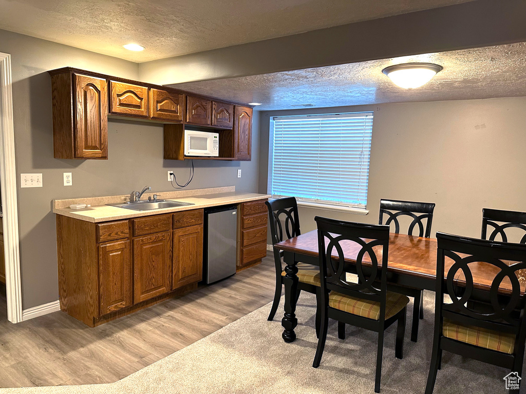 Kitchen featuring a sink, a textured ceiling, white microwave, light wood-style floors, and light countertops