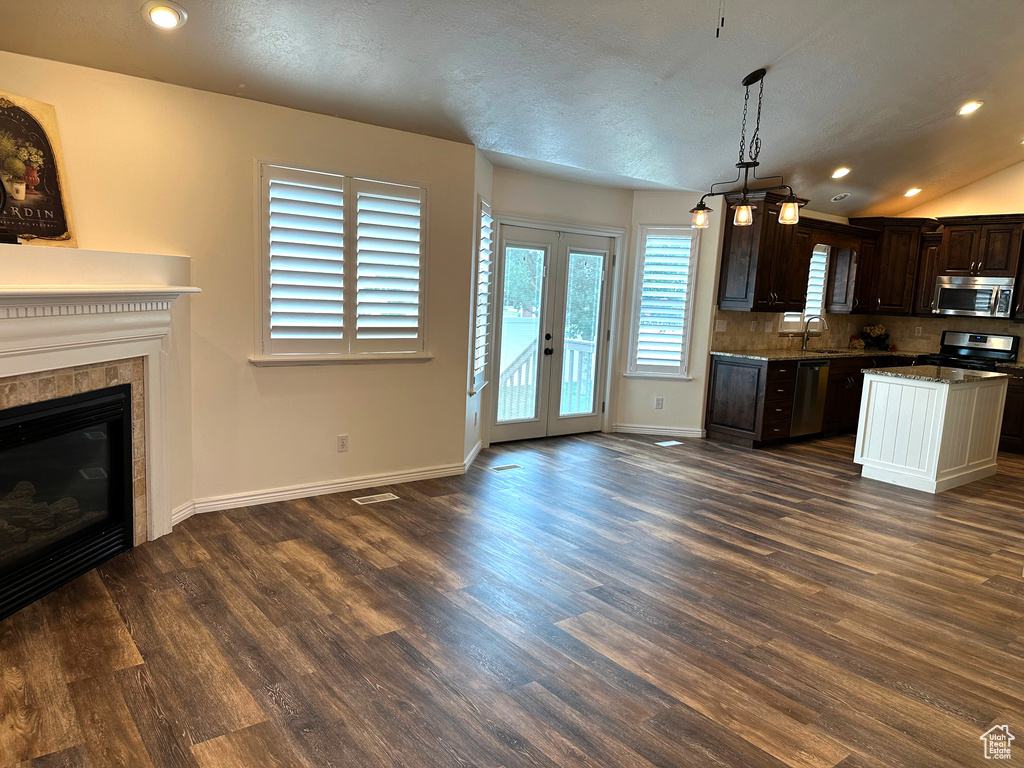 Kitchen with appliances with stainless steel finishes, a sink, dark brown cabinetry, dark wood-style flooring, and baseboards