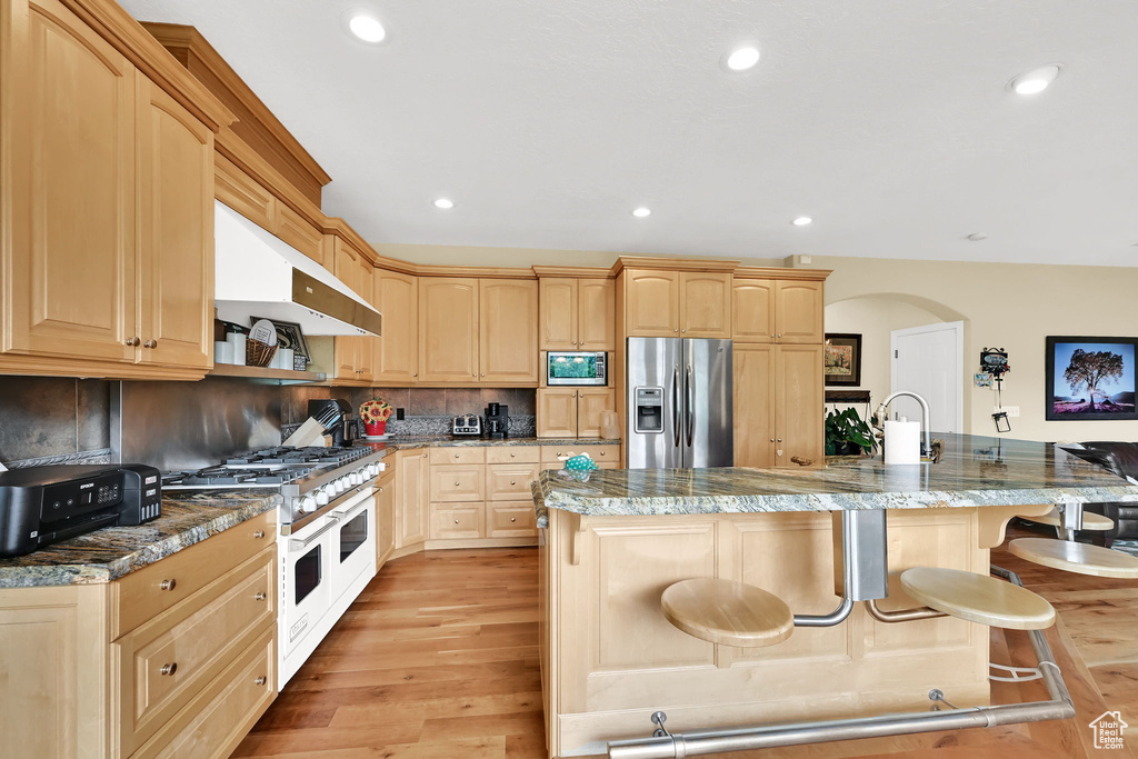 Kitchen with stainless steel appliances, light brown cabinetry, a breakfast bar, and recessed lighting