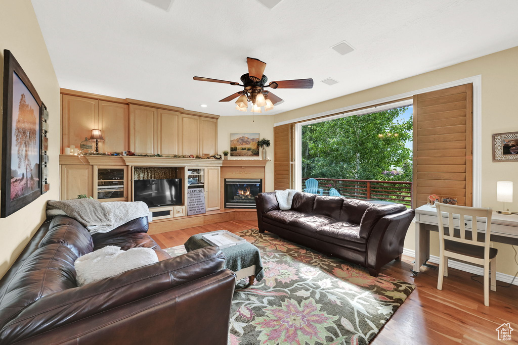 Living area with light wood-style flooring, ceiling fan, and a lit fireplace
