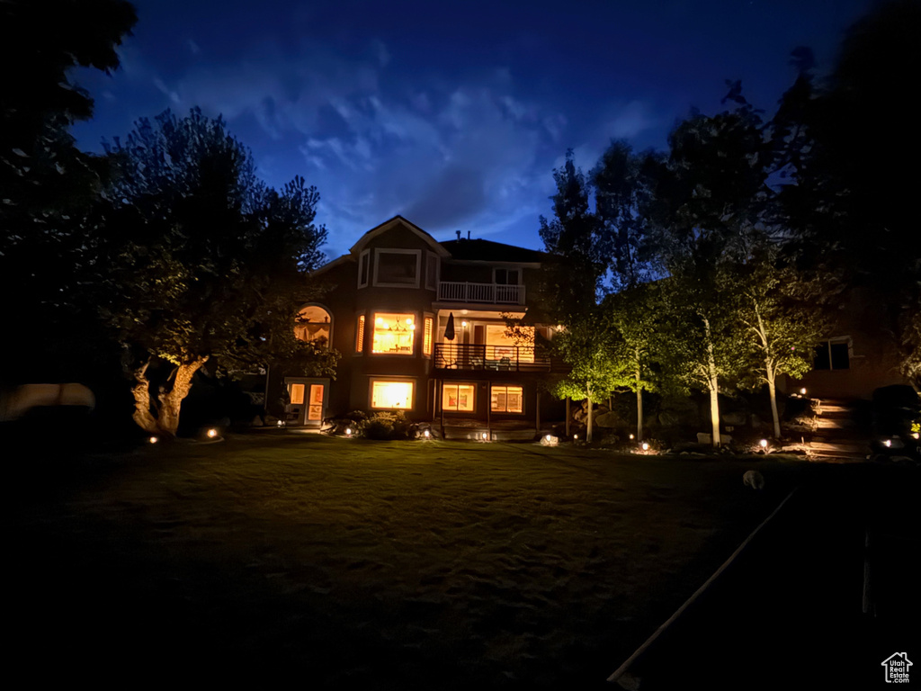 Back of house at twilight featuring a balcony and stucco siding