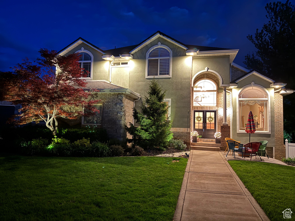 View of front of home with french doors, a lawn, and stucco siding