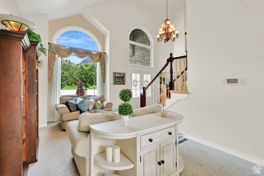 Carpeted living room with baseboards, a chandelier, stairway, and high vaulted ceiling