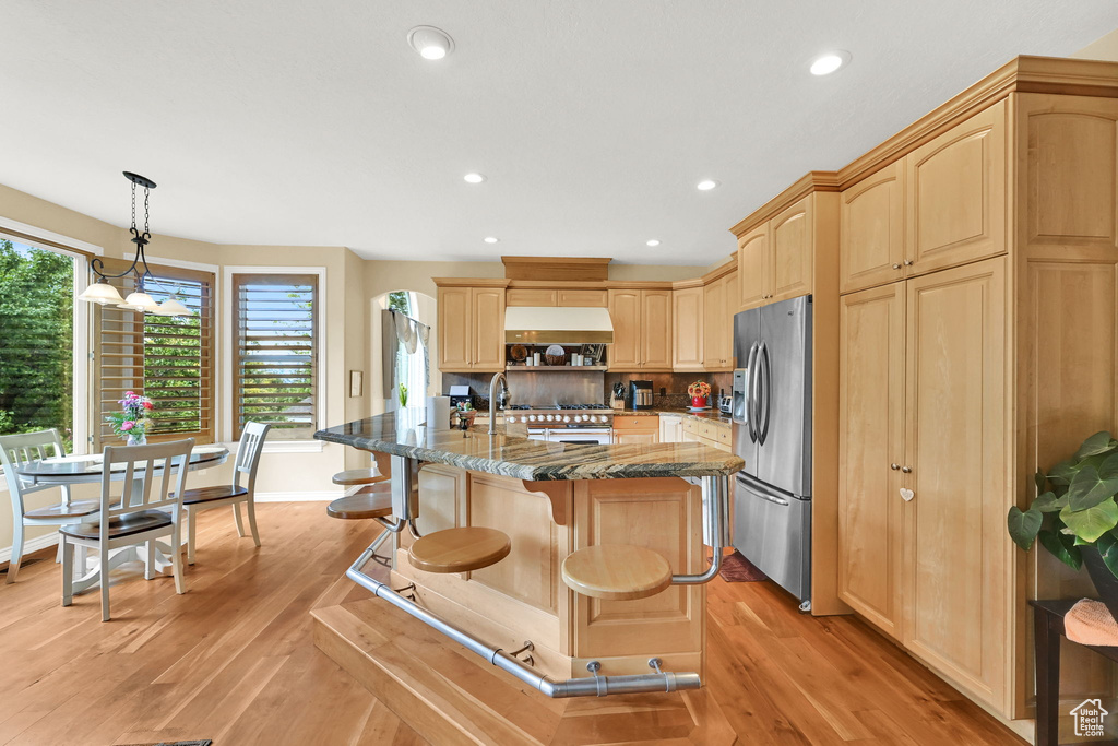 Kitchen featuring appliances with stainless steel finishes, light brown cabinets, light wood-type flooring, dark stone countertops, and a kitchen bar